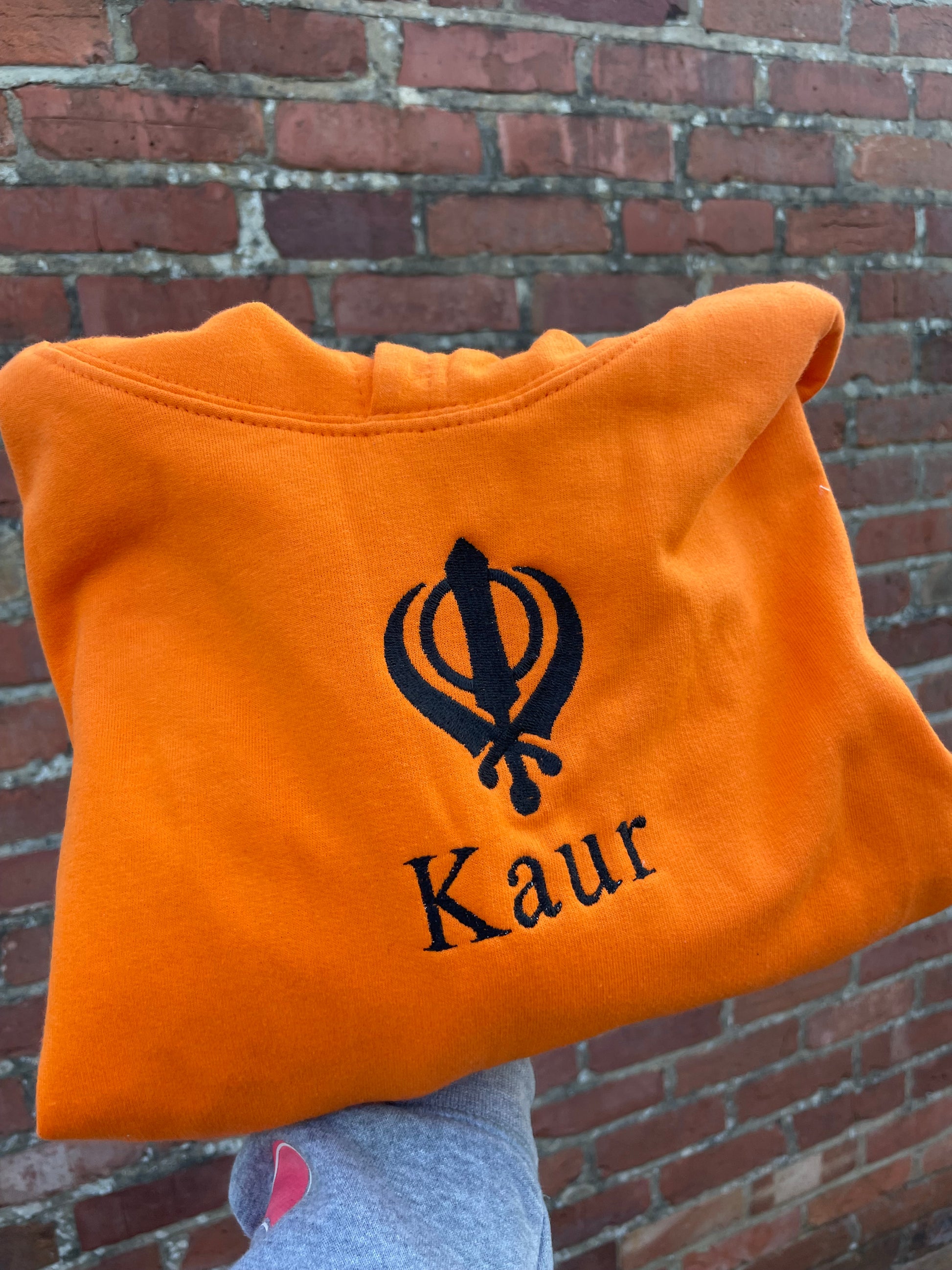 Experience ultimate style and grace with our Embroidered Kaur Orange hoodie. Made with intricate embroidery of the Kaur and Khanda, this hoodie exudes elegance and tradition. Elevate your wardrobe and embrace your identity with this unique and culturally significant piece.